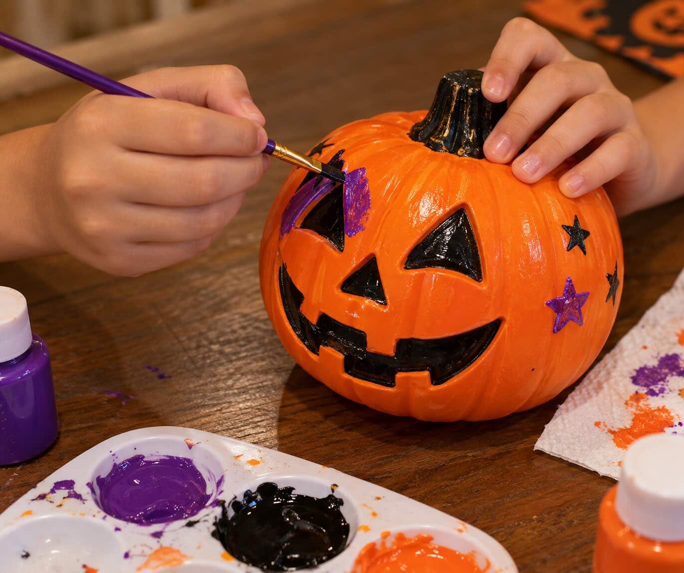Painting a jack-o'-lantern pumpkin with purple and black paint