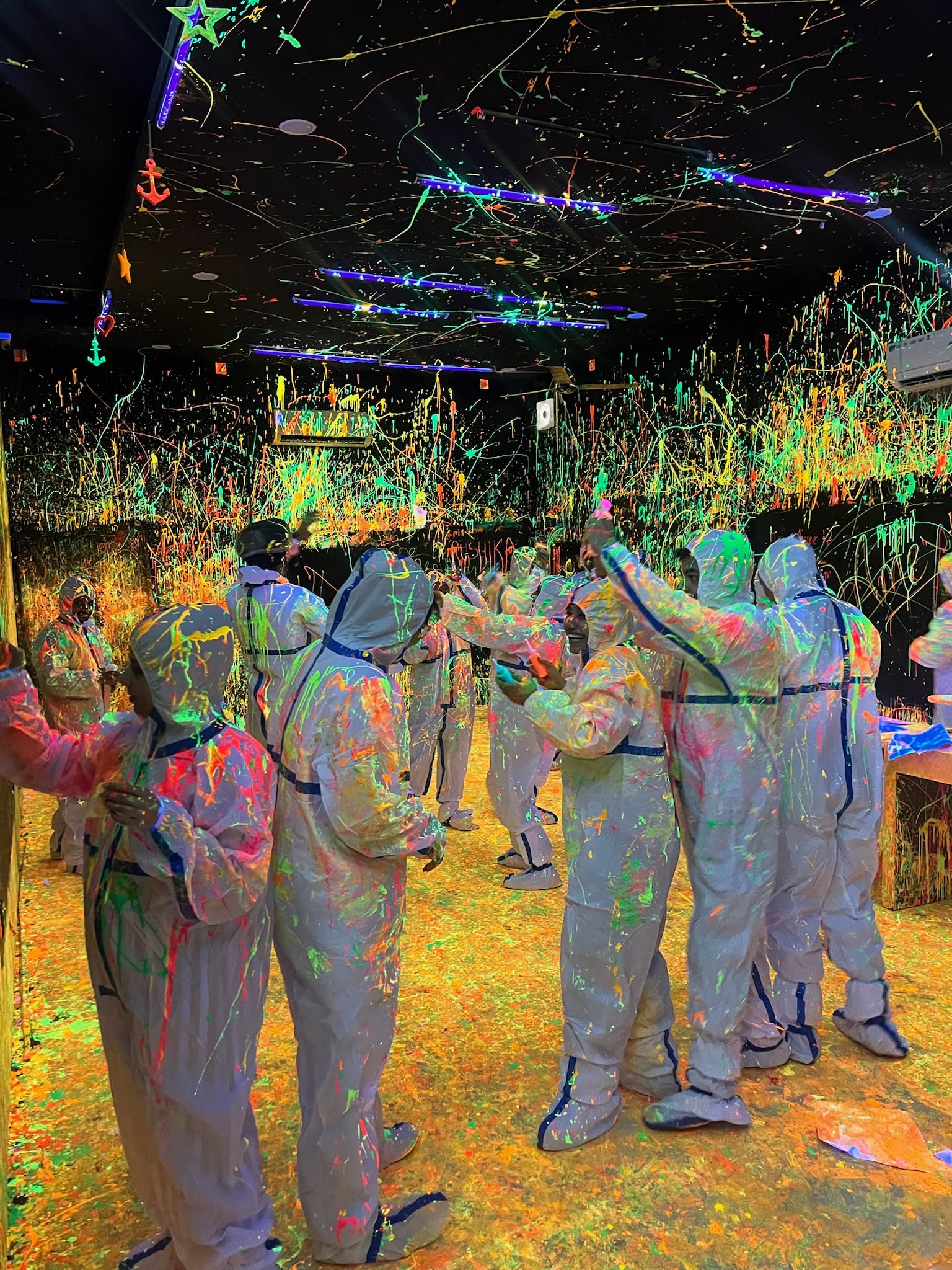 Friends throwing glow-in-the-dark neon paint in Splashit's UV blacklight splatter room